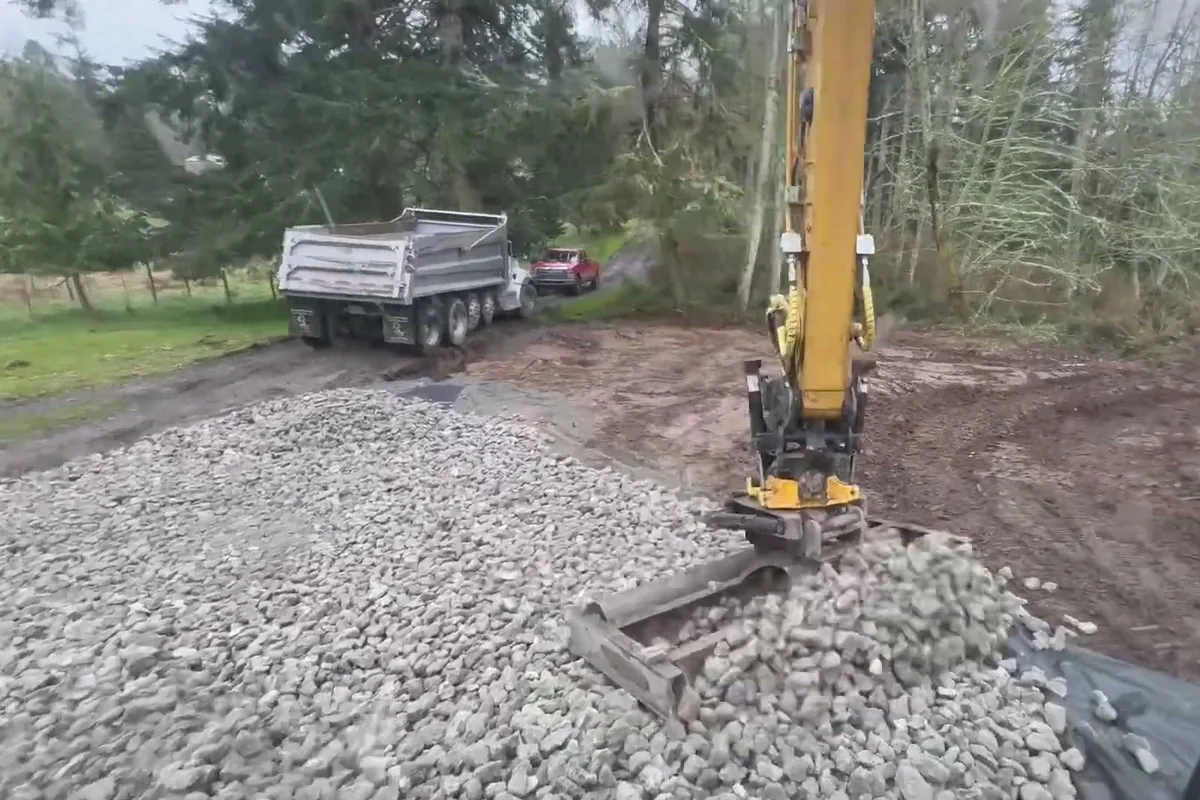 Crushed rock from the dump truck being spread across a gravel driveway with the excavator